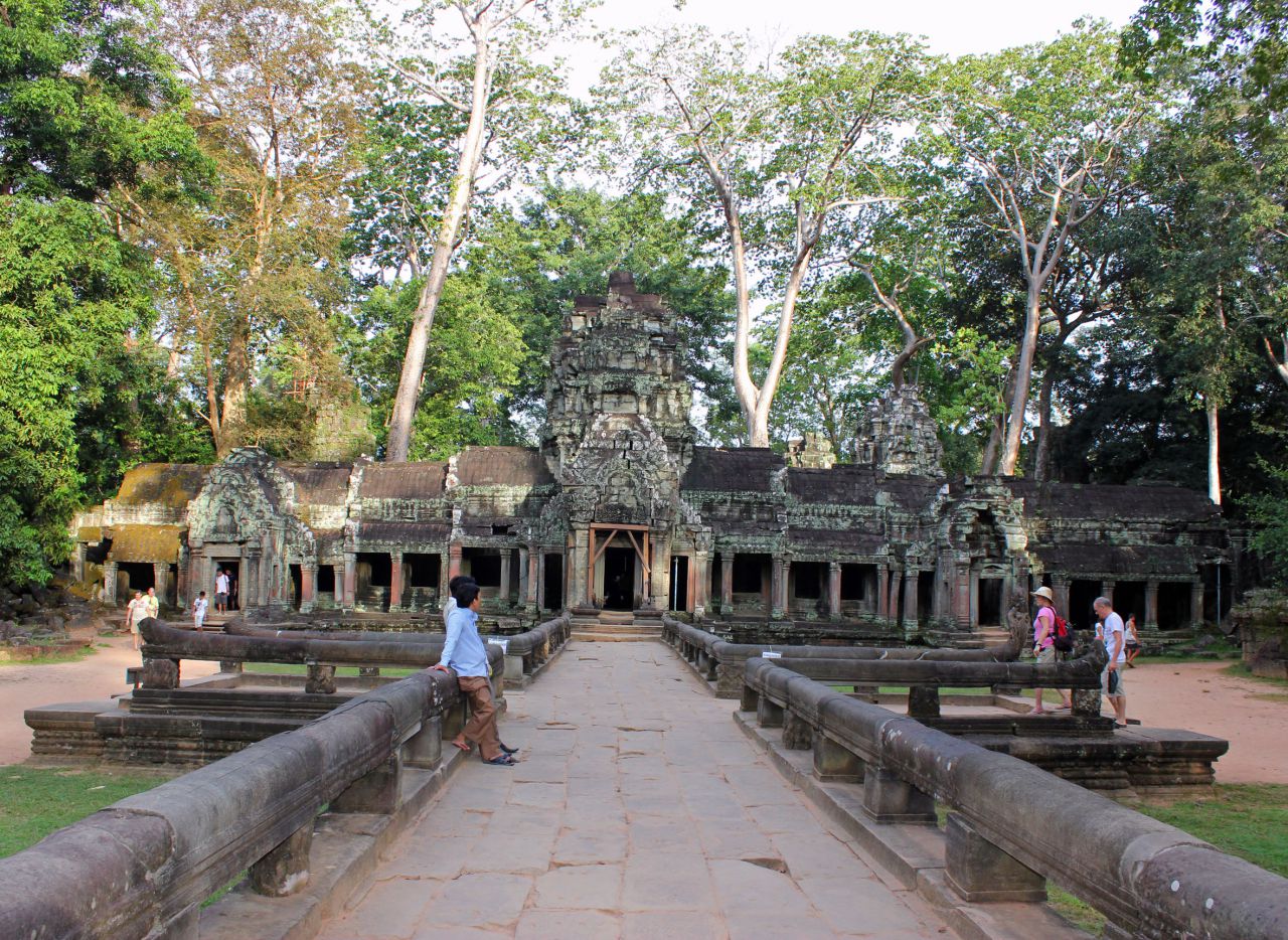 Храм Та-Пром, Ангкор, Камбоджа Храм Та Пром, как и Ангкор Ват, занимает большую территорию, но по архитектуре совершенно не похож на другие храмы Ангкора. Он состоит из цепочки одноэтажных длинных строений, соединенных между собой сквозными проходами и галереями. Та Пром обнесен внушительной стеной, но она не отделяет его от джунглей. Огромные деревья с лианами растут прямо среди зданий, обволакивая их своими мощными корнями, прорастают сквозь стены, разорвав камни. - Путешествие группы МироТворцев по Камбодже, декабрь 2012г.